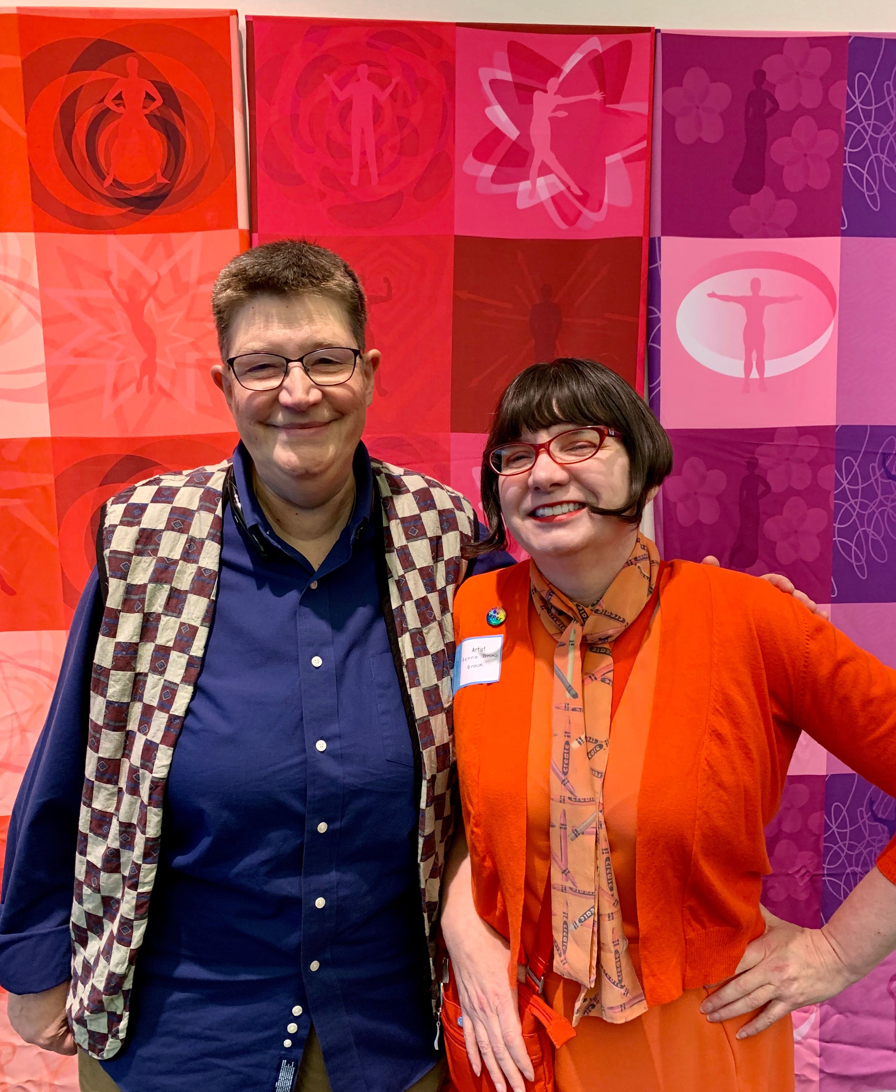Two women standing in front of colorful textile art